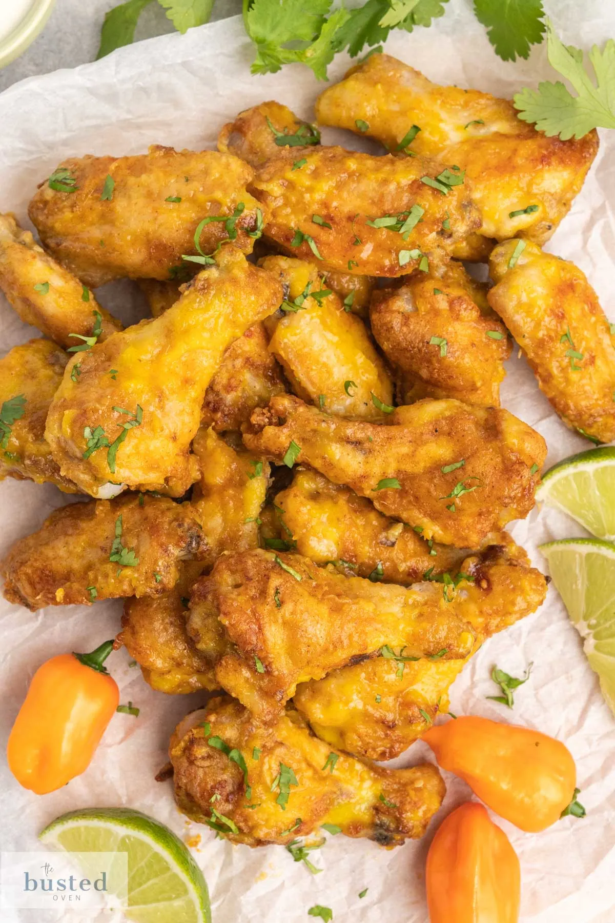 A platter of hot wings with whole habaneros and lime wedges on the side.