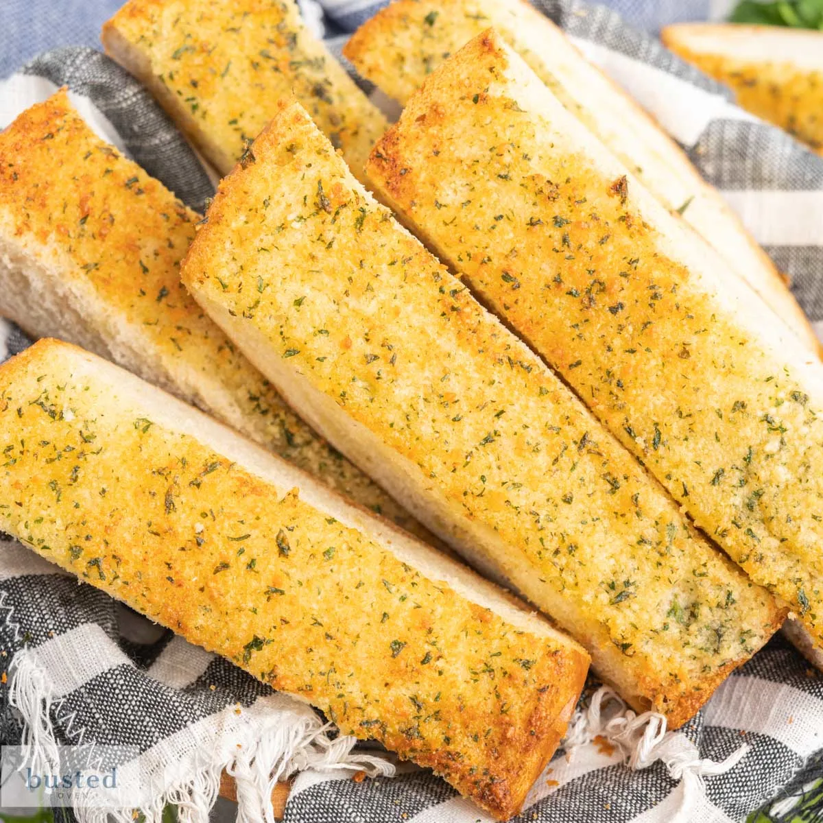 Slices of garlic bread in a basket lined with a striped cloth napkin.