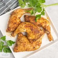 Four seasoned cooked chicken leg quarters on a square platter.