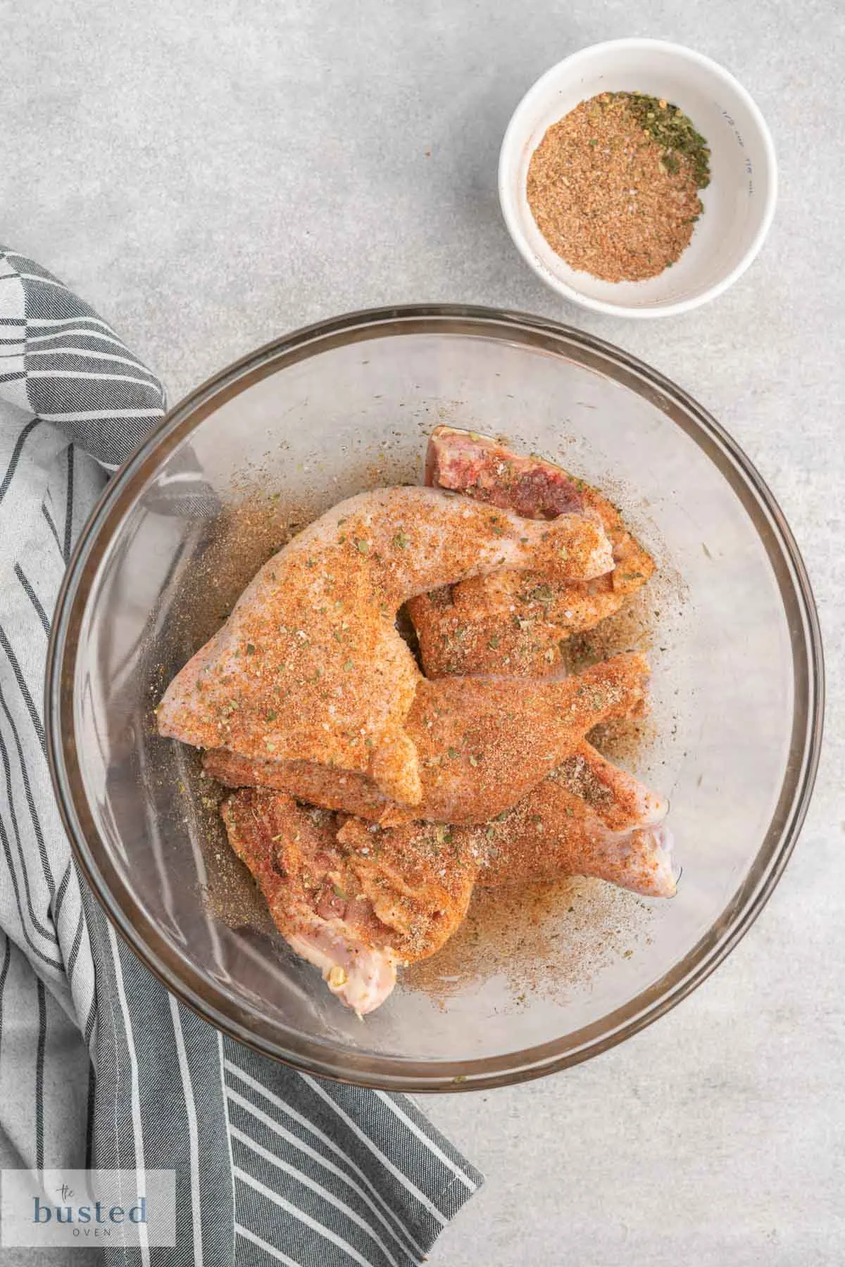 Chicken leg quarters coated in seasoning in a large bowl.