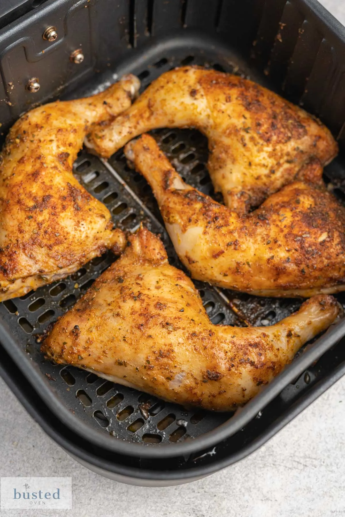 Cooked chicken leg quarters in an air fryer basket.