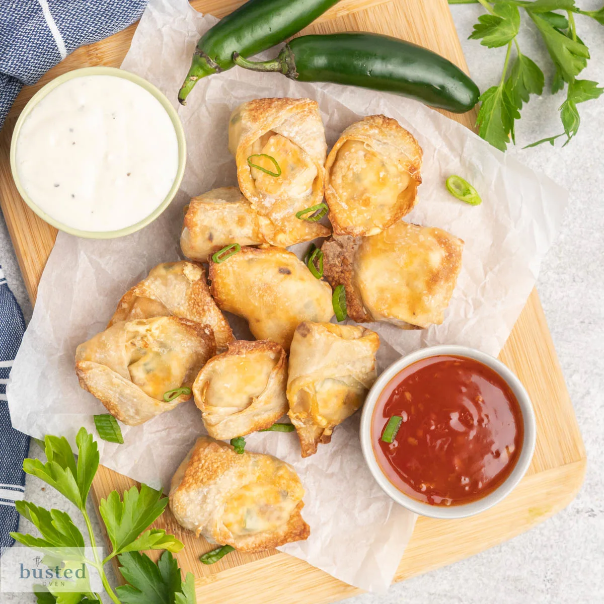 Jalapeno popper wontons on a serving platter with a dish of ranch dip and a dish of sweet chilli sauce.