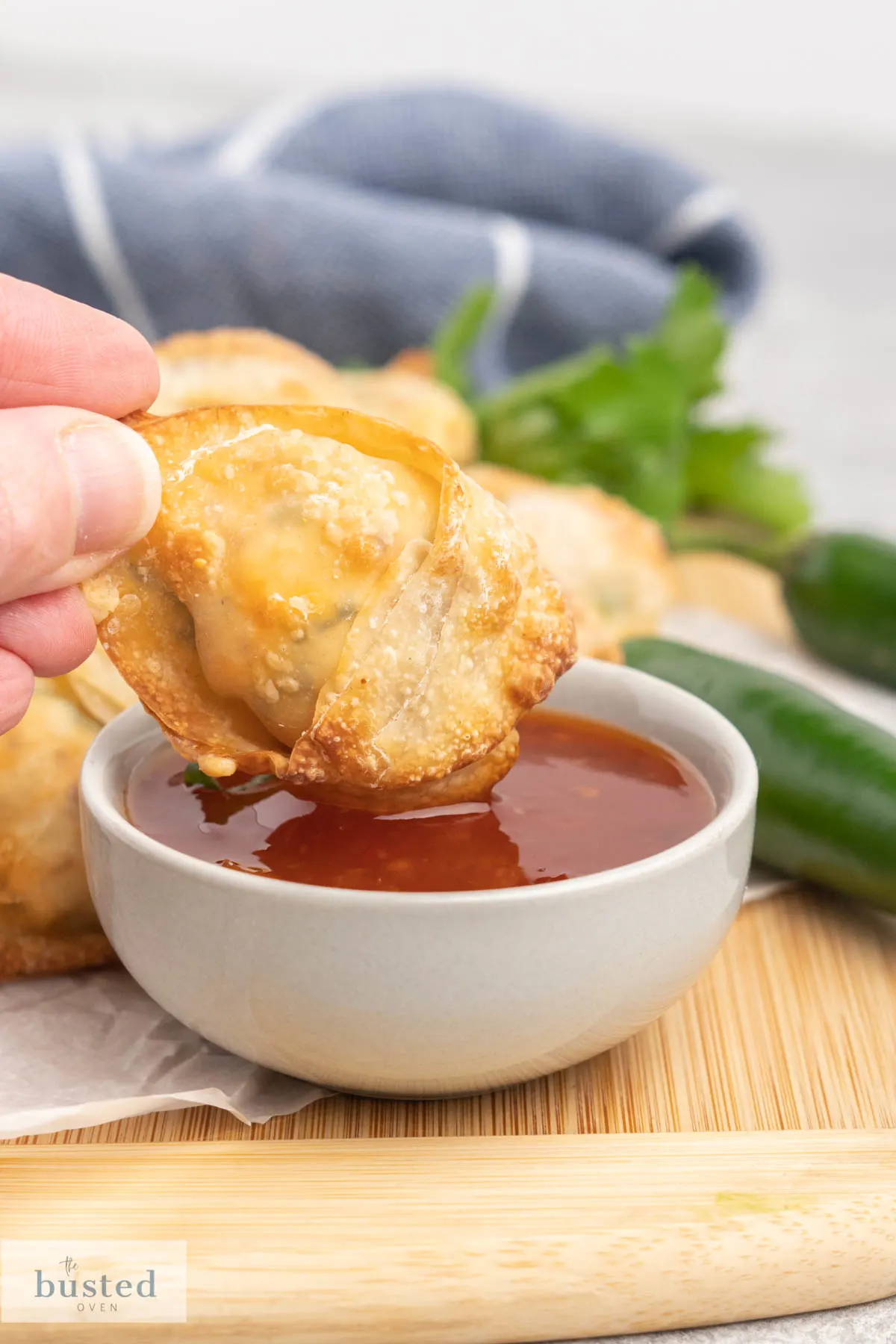 A crispy wonton being dipped in a dish of sweet chilli sauce.