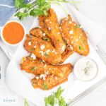 A plate of cooked turkey wings coated in buffalo sauce and sprinkled with blue cheese and fresh chopped parsley.